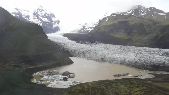 Iceland glacier wide shot with water, green grass and blue ice with drone video moving down.