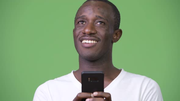 Young African Man Thinking While Using Phone Against Green Background