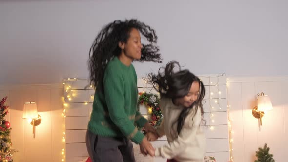 Happy African American Mom and Daughter Jumping on the Bed Against the Background of Christmas Tree