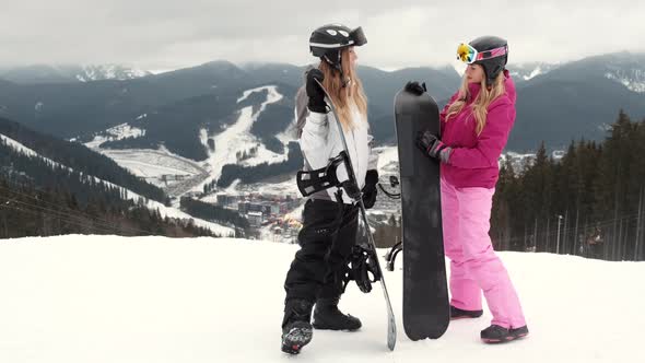Two Stylish Women with Their Snowboards on Mountain