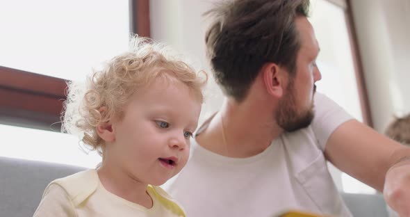 Closeup of a Little Girl and Her Bearded and Mustashed Father are Looking Pictures in Book Sitting