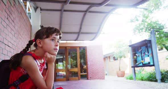 Sad schoolgirl sitting alone in corridor at school