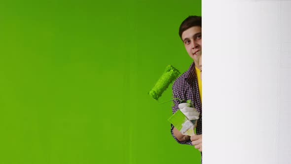 Smiling Man with a Woman Against a Green Wall, Looking Out From Behind a White Partition, Holding a