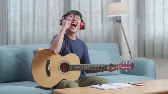 Asian Boy Composer Wearing Headphones With A Guitar Celebrating For Finishing Composing Music