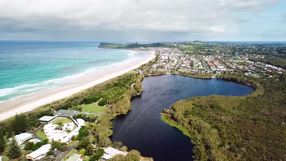 Drone flying in sideways arc showing freshwater tea-tree stained lake, adjacent beach and headland i