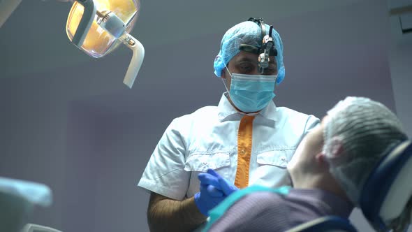 Professional Middle Eastern Dentist Talking to Patient in Dental Chair Rubbing Gloves with Sanitizer