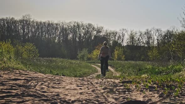 Young Woman on a Bicycle Rides Along Green Forest Path in Sunny Summer Day