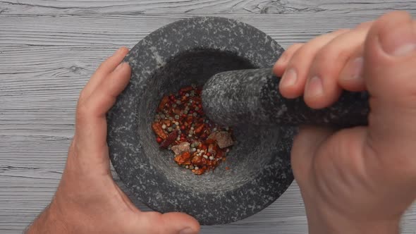 Top View of Hand with Heavy Pestle Starting to Grind Mix of Spices and Peppers