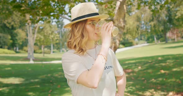 Young Caucasian Pretty Woman Wearing Stylish Hat Drinking Coffee in Green Park