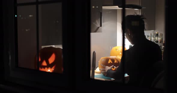 Woman carving pumpkin for Halloween night - View through the window of a youn