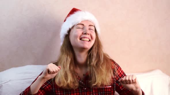 Young woman wearing santa hat is dancing sitting in bed