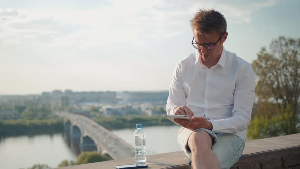 Young Man Sitting on Coastline Having Conversation with Voice Message Recorder on Smartphone Outside