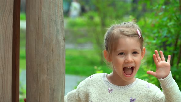 Girl Hides and Scares on Children Playground Smiles and Laughs in Green Summer Park