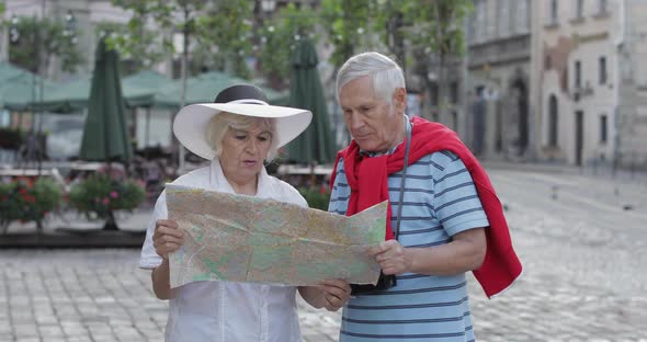 Senior Male and Female Tourists Standing with a Map in Hands Looking for Route
