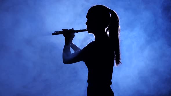 Woman in Spotlight in Smoky Studio Plays on Flute, Silhouette