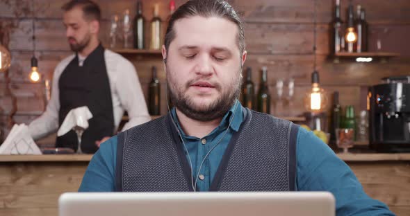 Young Businessman in a Small Coffee Shop Drinks Coffee During a Video Call