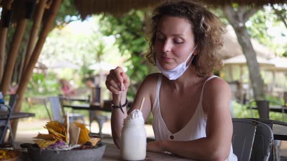 Caucasian Girl Takes Off Her Protective Face Mask to Try Whipped Cream of Her Milkshake During Lunch