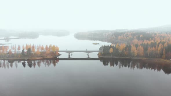 Aerial, drone shot, flying towards a bridge, surrounded by mist and autumn colors,, on a foggy, mist