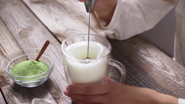 Soy Milk In Transparent Glass Cup Is Whipped On Wooden Kitchen Table. Preparation Of Matcha Tea