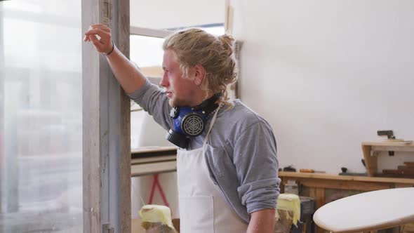 Caucasian male surfboard maker wearing a face mask and standing in his studio