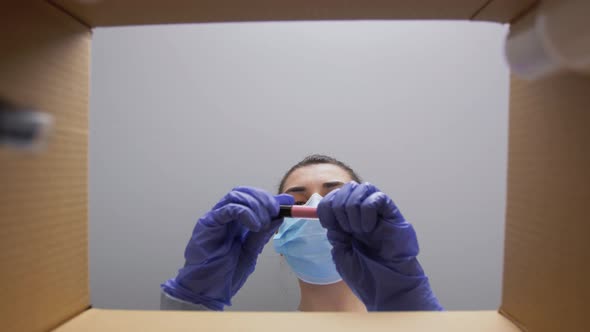 Woman in Mask Unpacking Parcel Box with Cosmetics