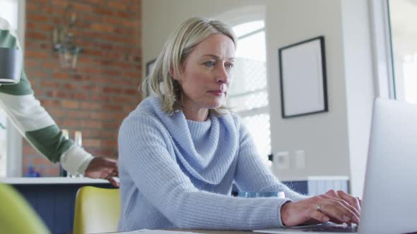 Stressed senior diverse couple in kitchen sitting at table, using laptop