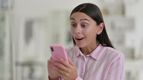 Excited Latin Woman Celebrating Success on Smartphone 