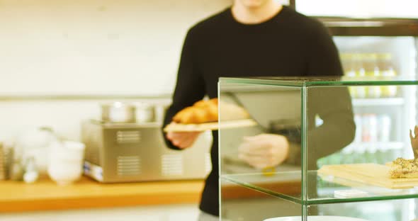 Man keeping tray of croissants in display case of coffee shop