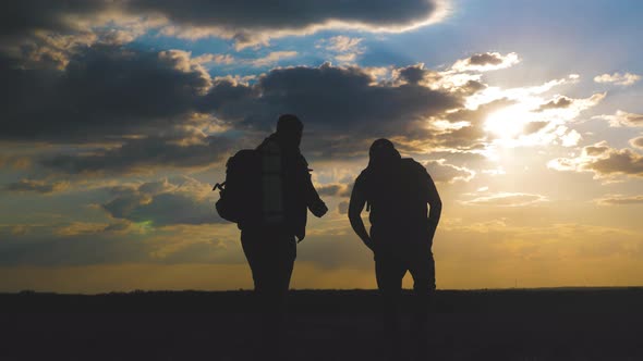Silhouettes of Two Hikers with Backpacks Enjoying Sunset View From Top of a Mountain. Enjoying the