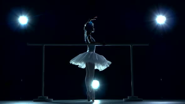Ballet Dancer in White Tutu on One Leg at Ballet Barre on a Blue