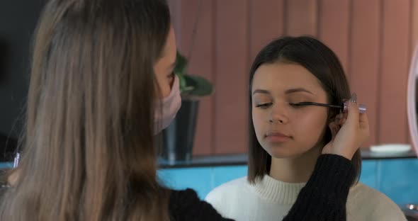 Female MakeUp Artist in Protection Mask Using Working with the Eyelashes of Client Young Woman on