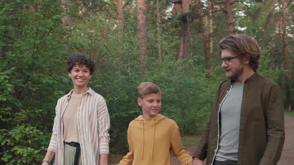 Young Family Of Three Strolling In Forest