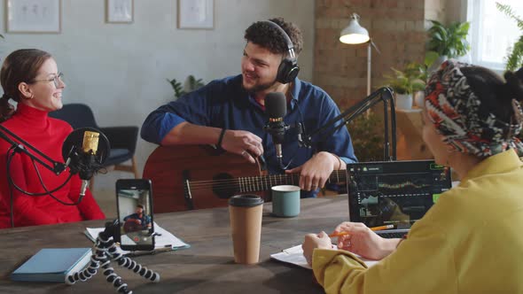 Two Female Hosts Interviewing Male Singer in Podcast Studio