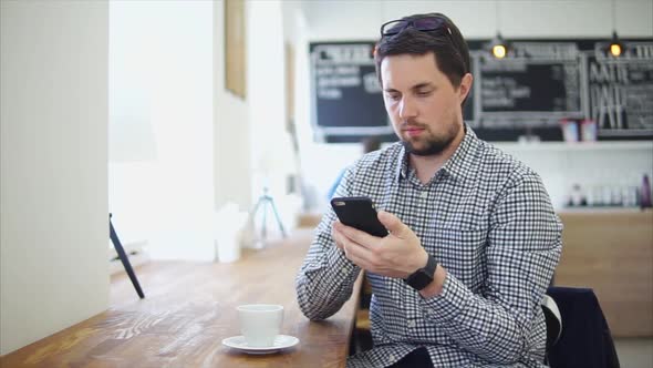 An Adult Man Communicates on the Phone Sitting in a Coffee House