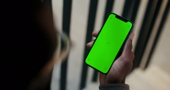 An African American Man Holds a Mobile Phone with a Green Screen in His Hand