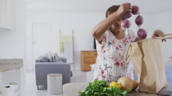 Happy african american senior woman in kitchen unpacking food from shopping bag, smiling