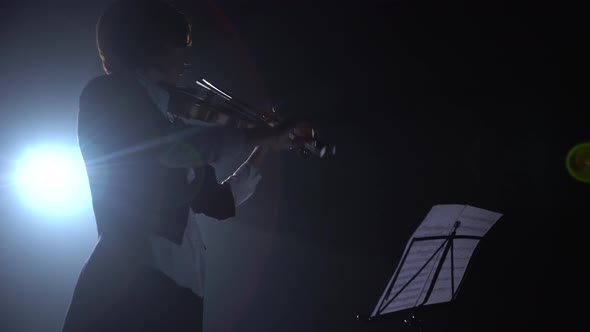 Violinist Looks at the Notes and Plays . Silhouette. Black Smoke Background