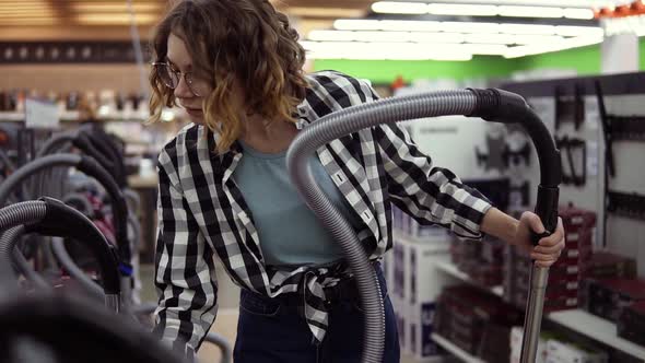 Pretty Curly Haired Woman Standing Near New Vacuum Cleaners in Home Appliance Store Take One to