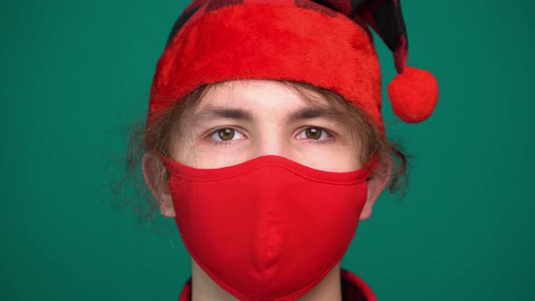 Portrait of Boy in Santa Hat Wears a Red Medical Mask Looking at Camera