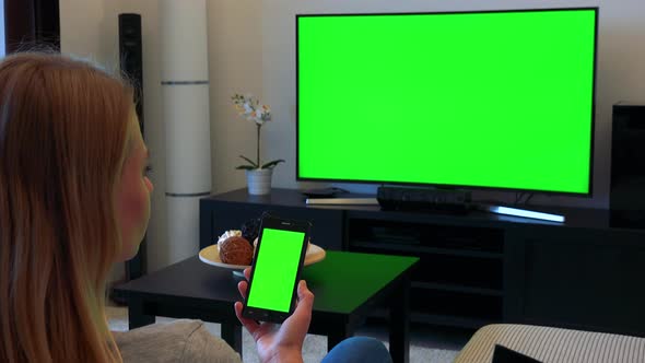 Woman Sits on Couch in Living Room and Works on Green Screen Phone and Watches TV