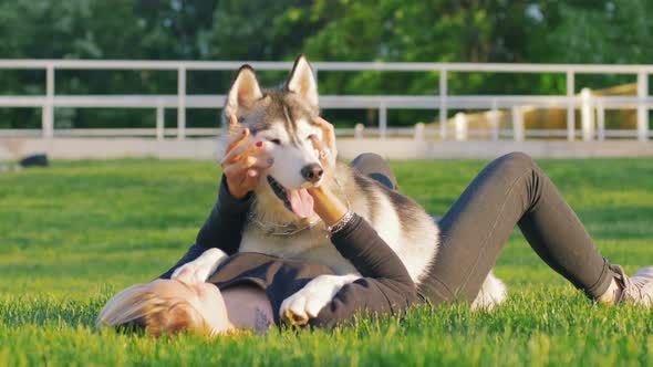 Beautiful Young Woman Playing with Funny Husky Dog Outdoors in Park