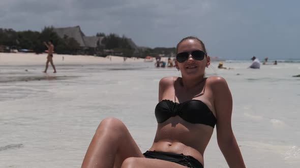 Young Woman in Black Bikini Tans on a Paradise White Sandy Beach Lies By Ocean