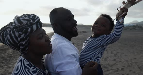 African parents and little son having fun with wood airplane on the beach