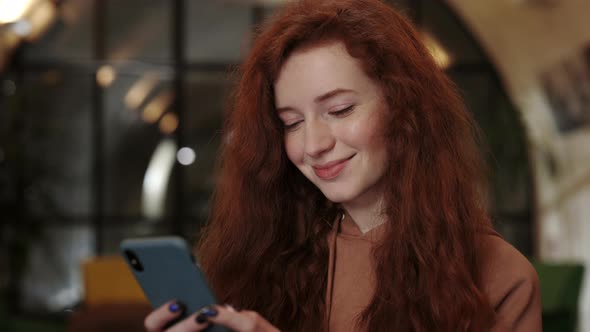 Close Up View of Young Female Person with Long Red Curly Hair Using Smartphone While Browsing