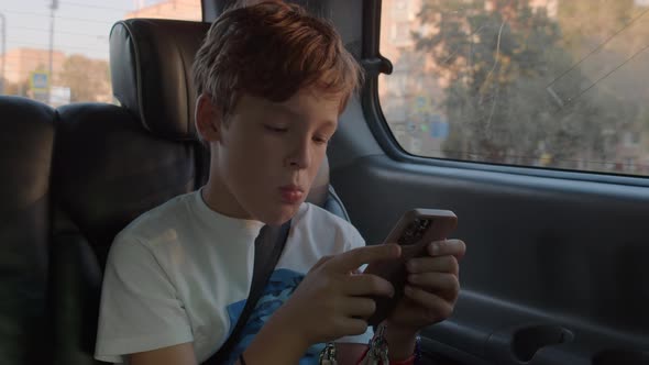 Boy Filling in Time with Phone During Car Ride