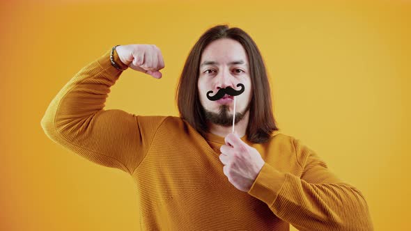 Funny Muscular Caucasian Bearded Man Holding Fake Paper Moustache and Tightening His Muscles