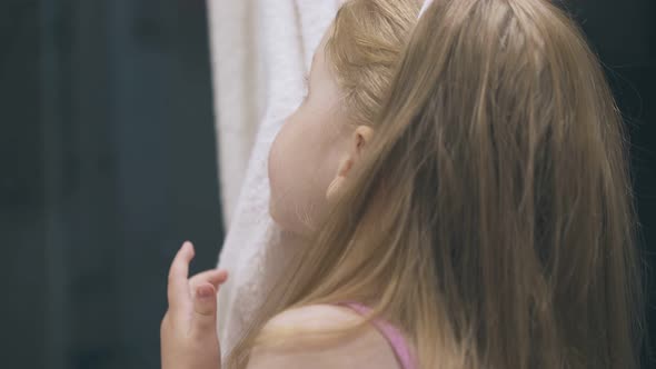 Little Girl Wipes Face with Soft Towel in Light Bathroom