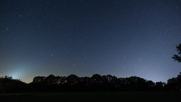 moving night sky over rural landscape with field in front of trees