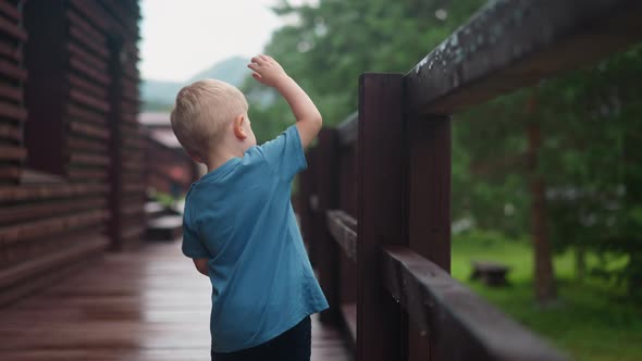 Curious Little Boy Touches Wet Wooden Railing on Deck