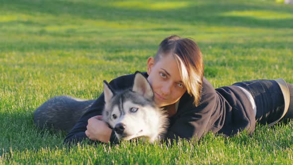 Beautiful Young Woman Playing with Funny Husky Dog Outdoors in Park